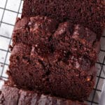 Three thick slices of moist chocolate zucchini bread are arranged on a black wire cooling rack, showing a rich, fudgy texture and a deep brown color.