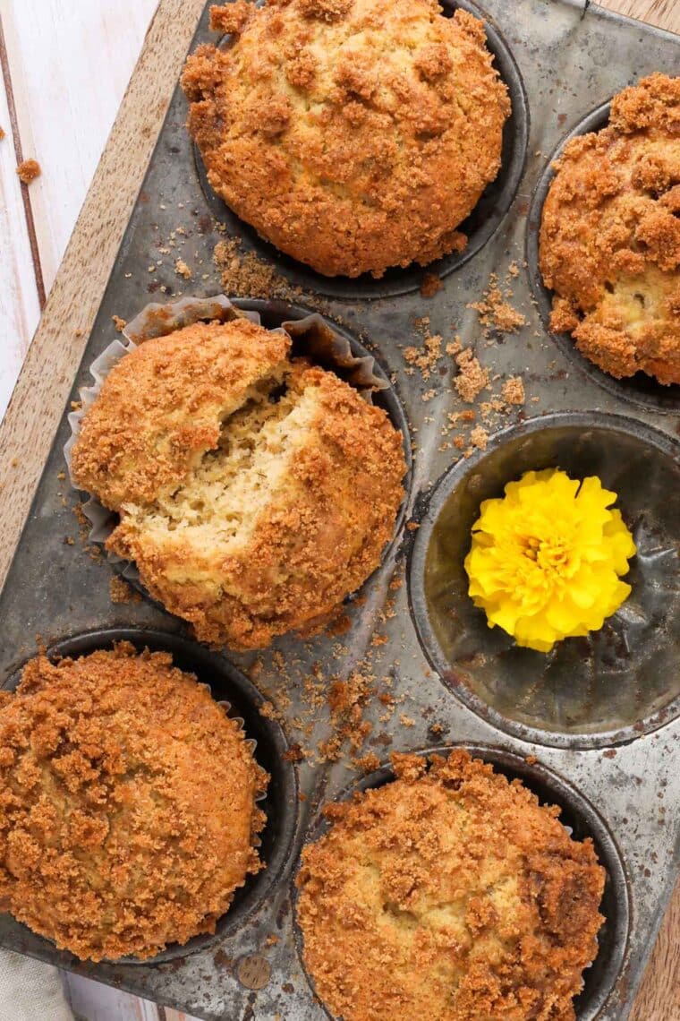 banana crunch muffin recipe in a tin on a cutting board with yellow marigolds