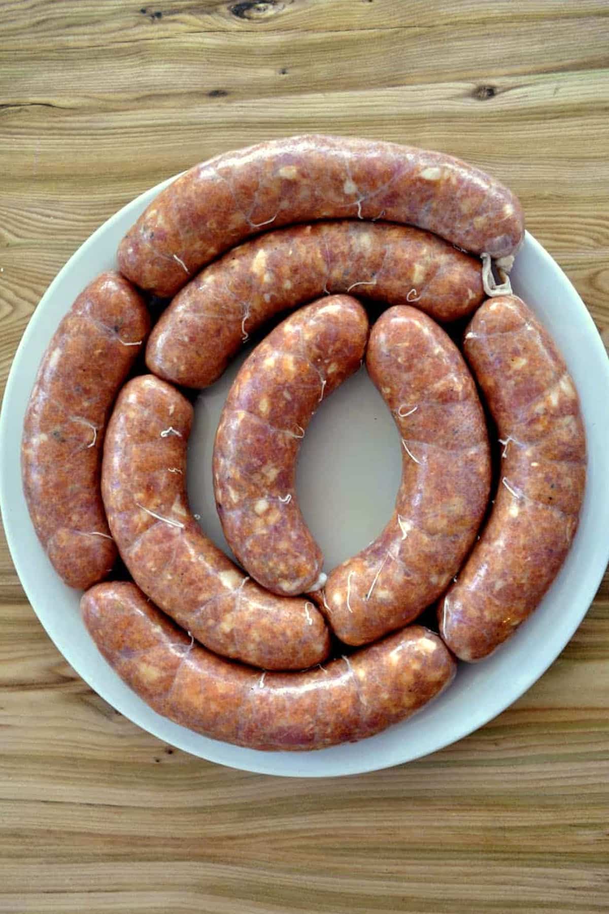 A white plate holds several uncooked homemade linguica sausages arranged in a spiral on a wooden table.