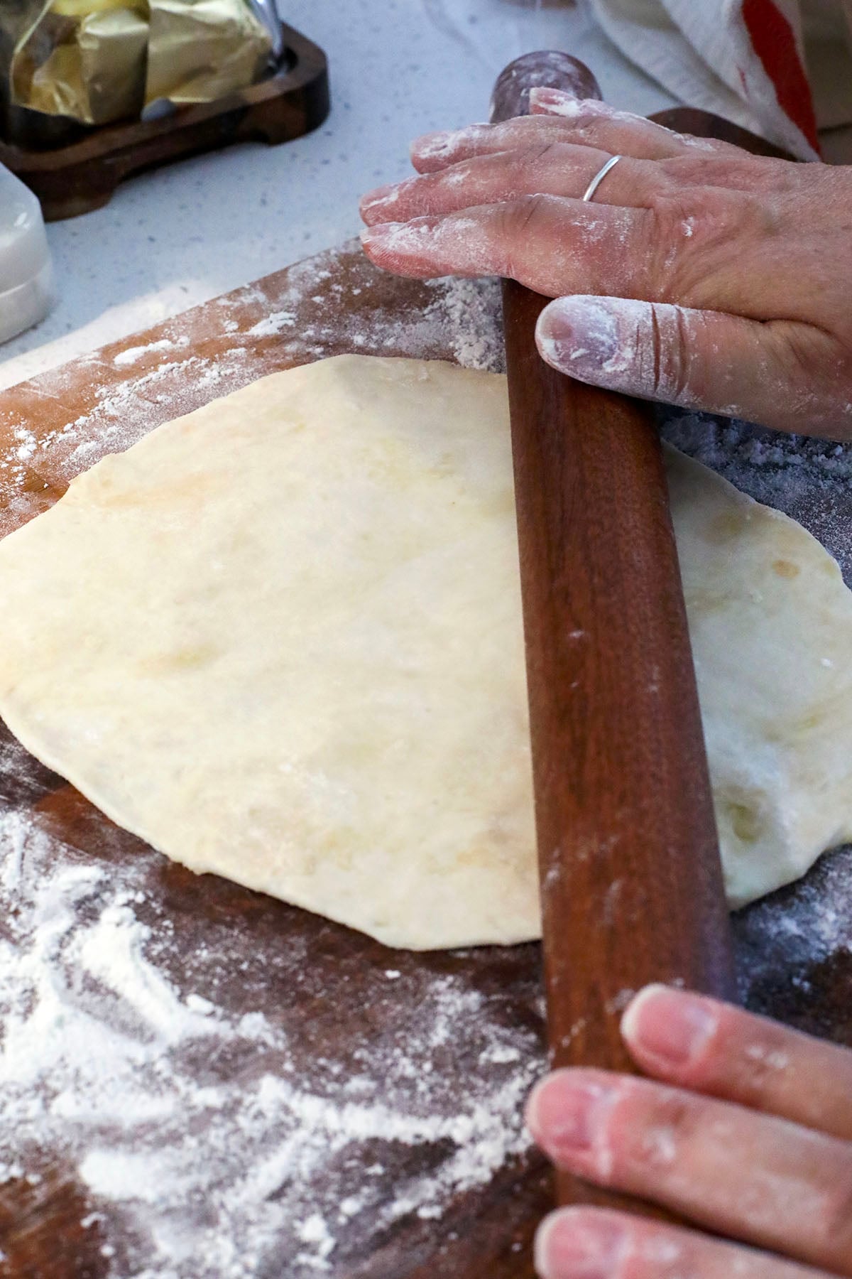 A clear glass bowl filled with ingredients for homemade flour tortillas—flour, baking powder, salt, and sugar—sits on a marble countertop next to a measuring cup containing oil.