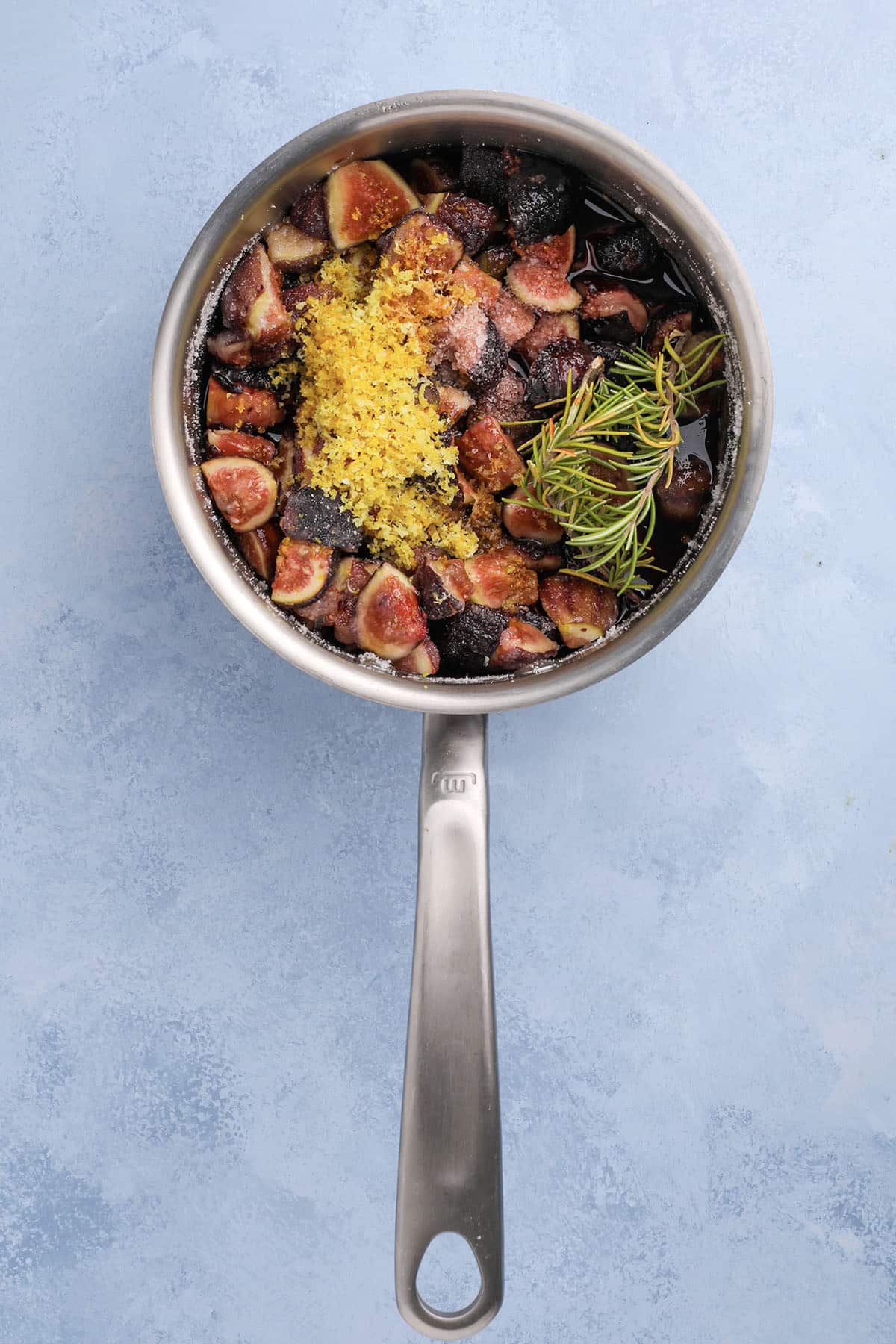 close-up of figs, rosemary, lemon zest, and port wine in a saucepan.