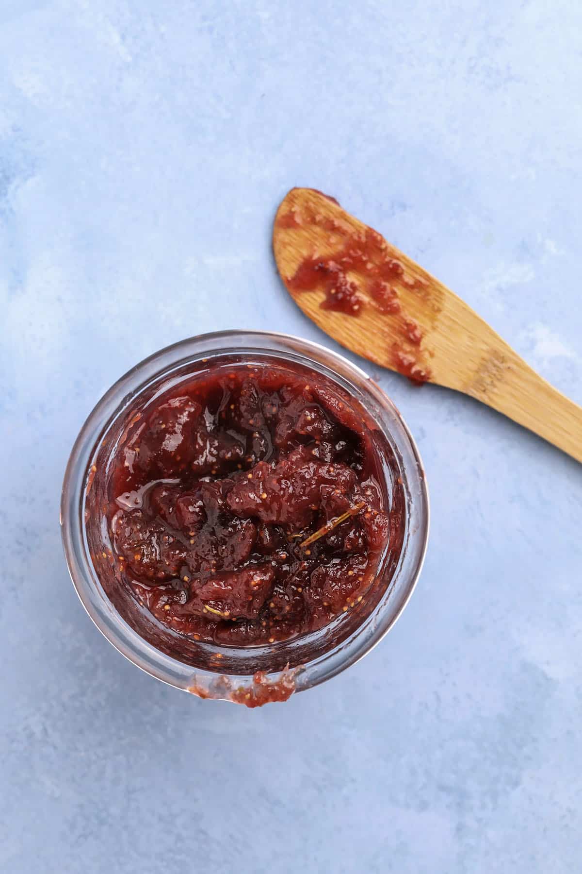 overhead shot of rosemary fig jam in a jar with a wooden spoon