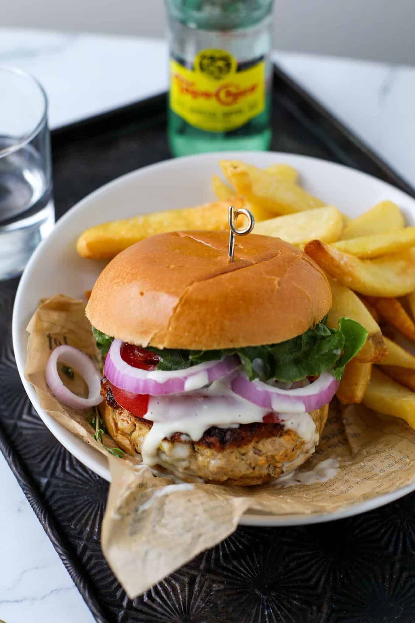 buffalo chicken burger on a plate with fries and a cold beverage