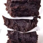 A stack of three thick, fudgy chocolate stout brownies separated by pieces of white parchment paper, set against a plain white background.