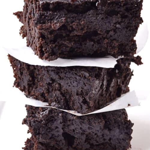 A stack of three thick, fudgy chocolate stout brownies separated by pieces of white parchment paper, set against a plain white background.