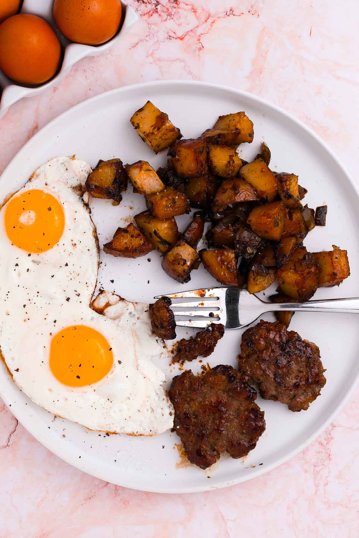 A plated breakfast with maple brown sugar sausage, fried eggs, and potatoes.