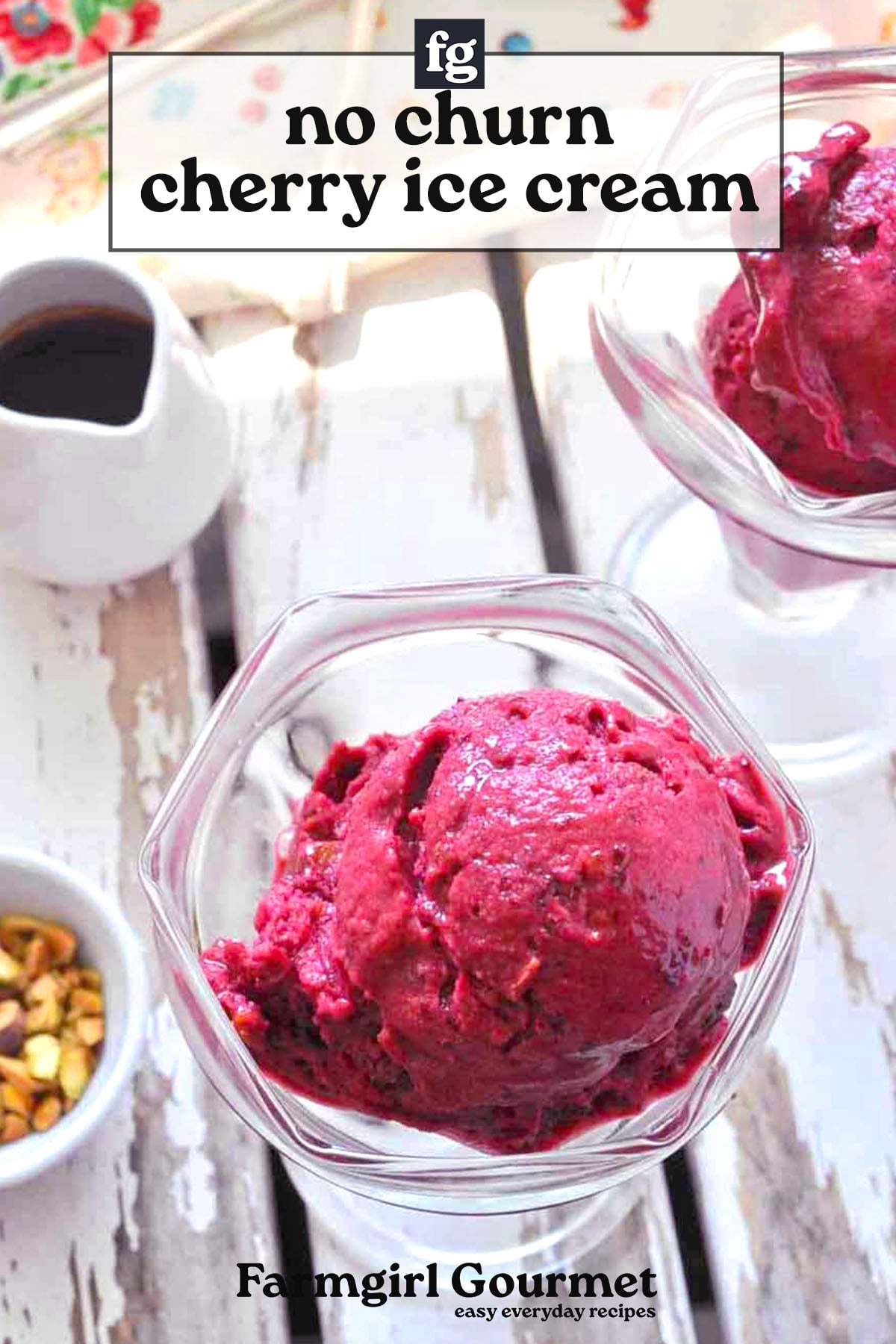 Two glass bowls filled with scoops of dark pink quick cherry ice cream sit on a white wooden table, with a jug of sauce and a small bowl of chopped nuts nearby. Text reads: “no churn cherry ice cream.”.
