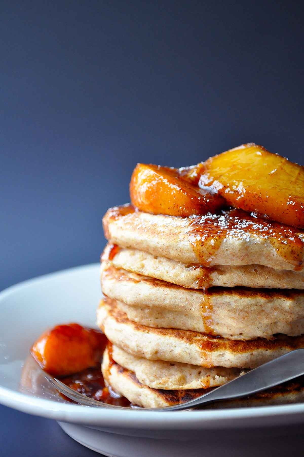 close up of applesauce pancakes with fresh peaches and syrup drizzling down the side