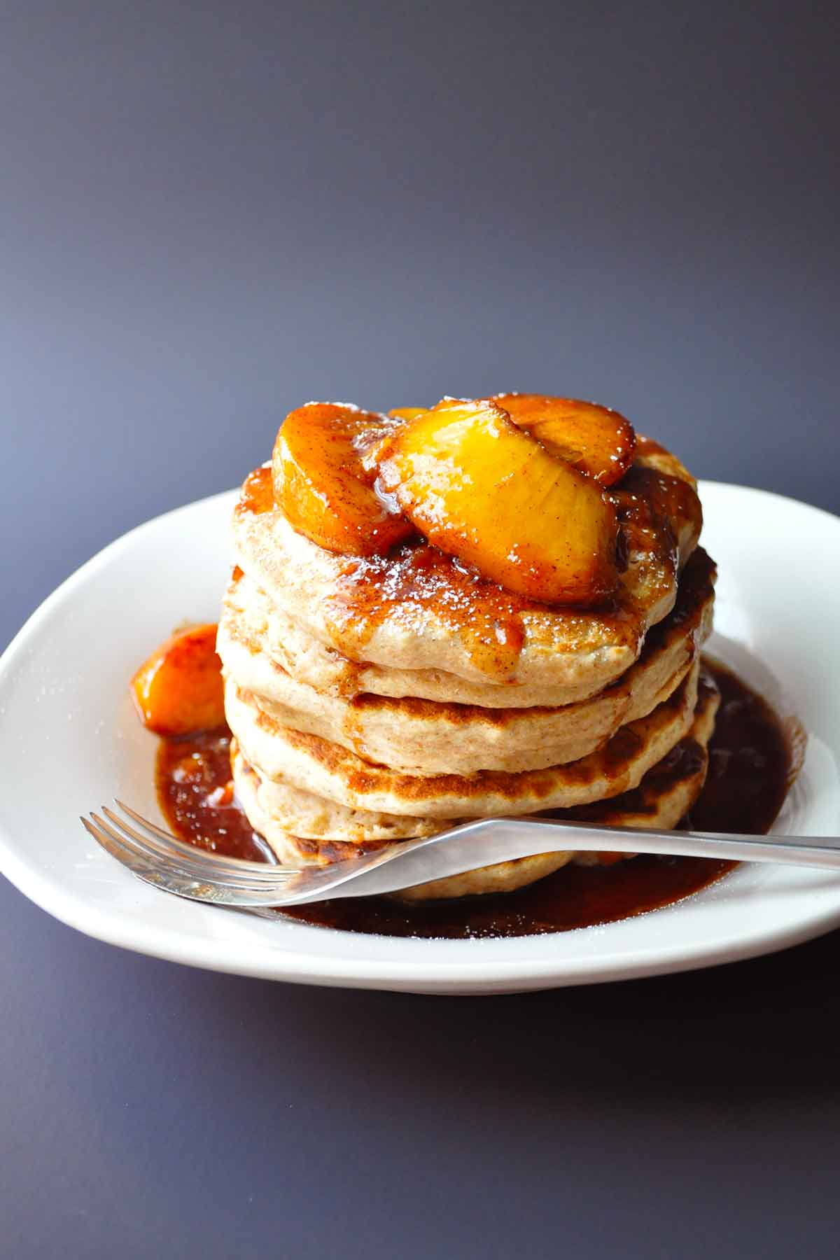 fresh peaches cooked with brown sugar and spices topping a pile of fluffy applesauce pancakes