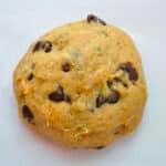 A round ball of raw Zucchini Chocolate Chip Cookie dough with visible chocolate chips and green flecks, resting on a plain white surface.