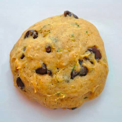 A round ball of raw Zucchini Chocolate Chip Cookie dough with visible chocolate chips and green flecks, resting on a plain white surface.