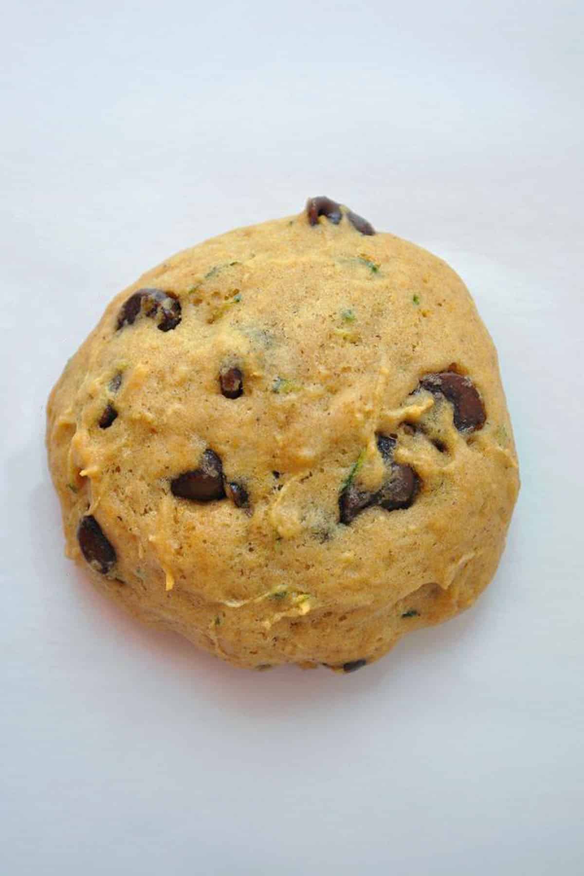 A round ball of raw Zucchini Chocolate Chip Cookie dough with visible chocolate chips and green flecks, resting on a plain white surface.