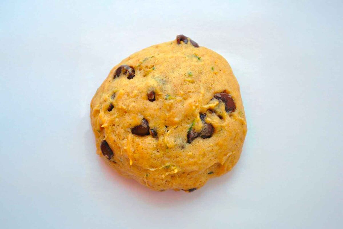 A single round Zucchini Chocolate Chip Cookie dough ball with a slightly orange tint, resting on a plain white surface.
