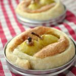 Seckel pear tarts with golden crusts and cinnamon sticks in the center, placed in round baking molds on a red and white checkered cloth.