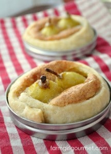 Seckel pear tarts with golden crusts and cinnamon sticks in the center, placed in round baking molds on a red and white checkered cloth.