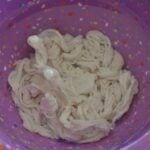 A colorful purple bowl with confetti-like specks contains a white, twisted, and slightly soapy mass of yarn or fabric soaking inside—resembling homemade linguica waiting to be prepared.