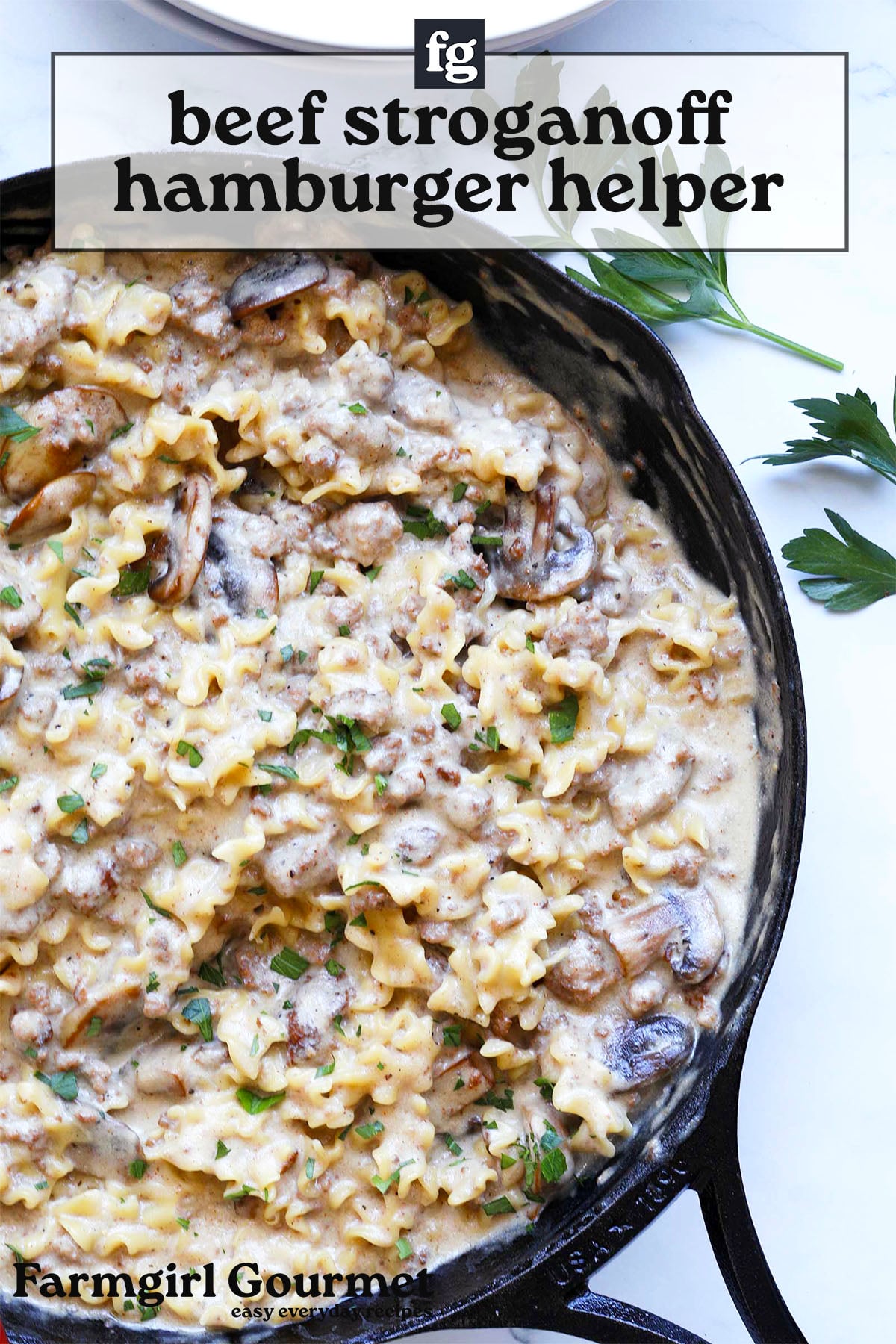 A cast iron skillet filled with creamy beef stroganoff hamburger helper, garnished with chopped parsley and served next to a sprig of fresh parsley. Text overlay reads beef stroganoff hamburger helper.