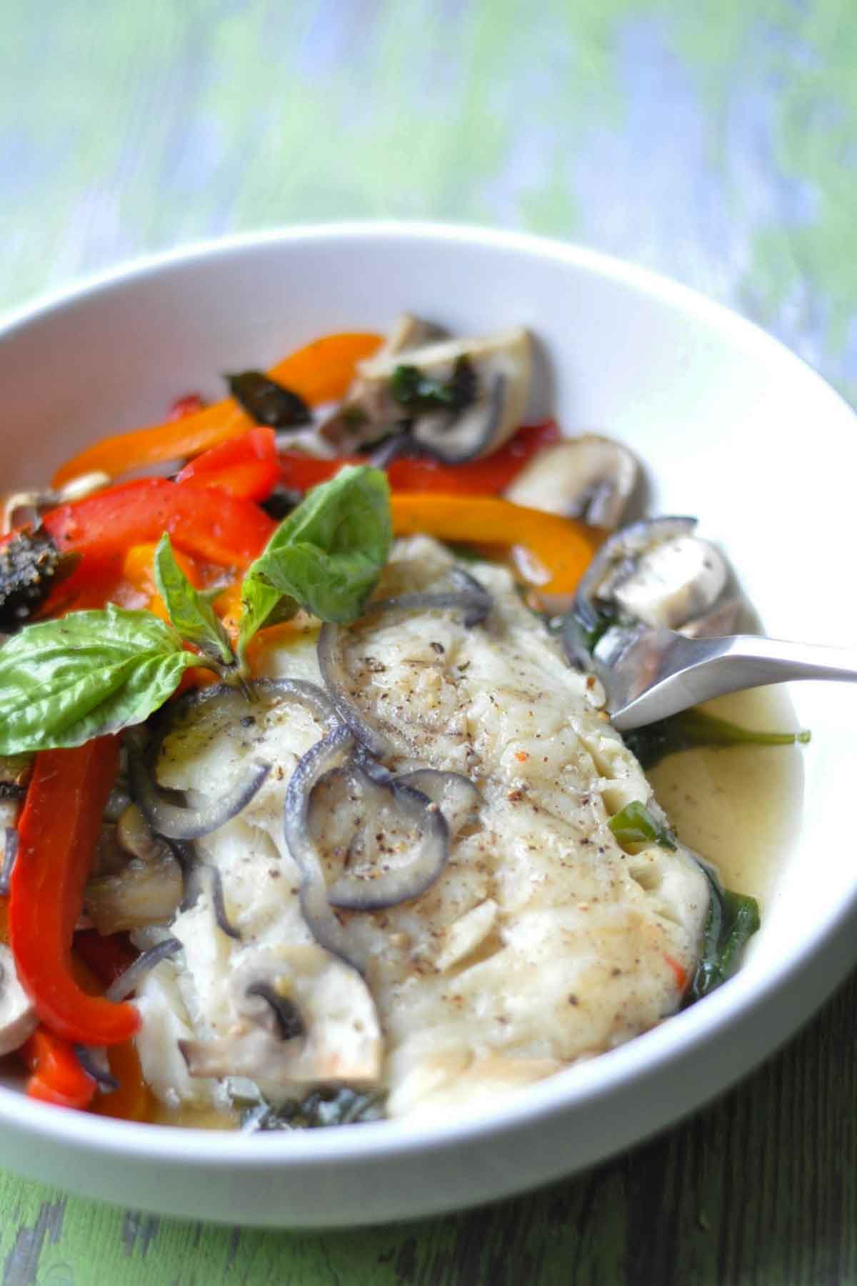 a bowl of cooked cod with vegetables in a white bowl