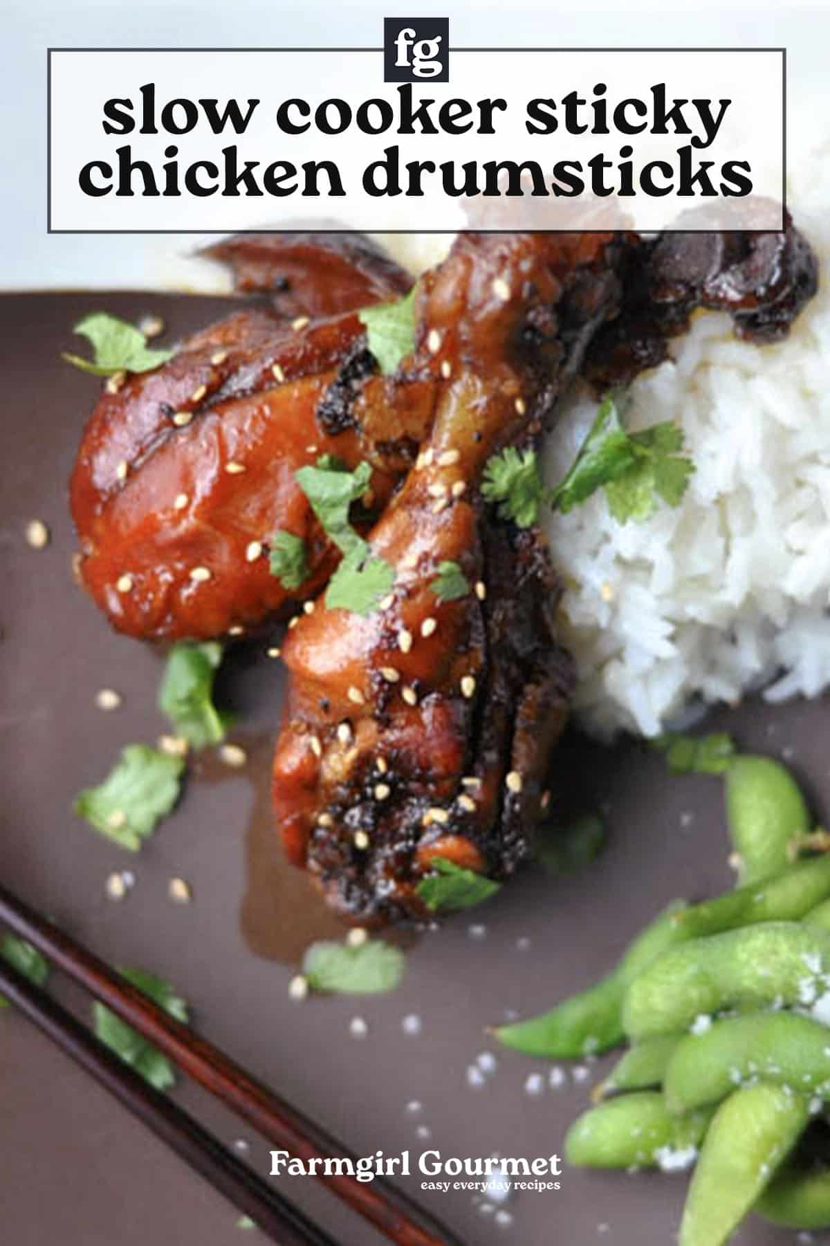 Close-up of succulent chicken drumsticks glazed in a sticky sauce, garnished with herbs and sesame seeds, served with white rice and edamame on a brown plate. Text overlay reads Slow Cooker Sticky Chicken Drumsticks.
