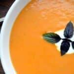 bowl of creamy chipotle tomato soup garnished with sour cream and fresh basil