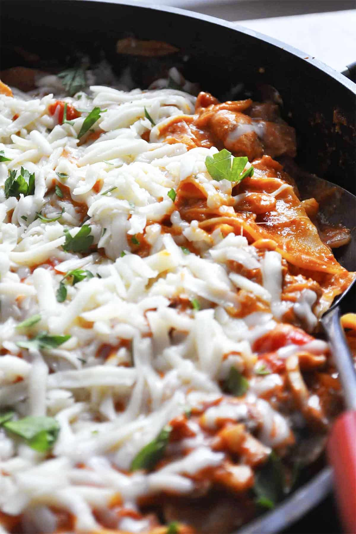 Close-up of skillet lasagna, filled with melted mozzarella cheese, rich tomato sauce, fresh parsley, and distinct pasta layers.