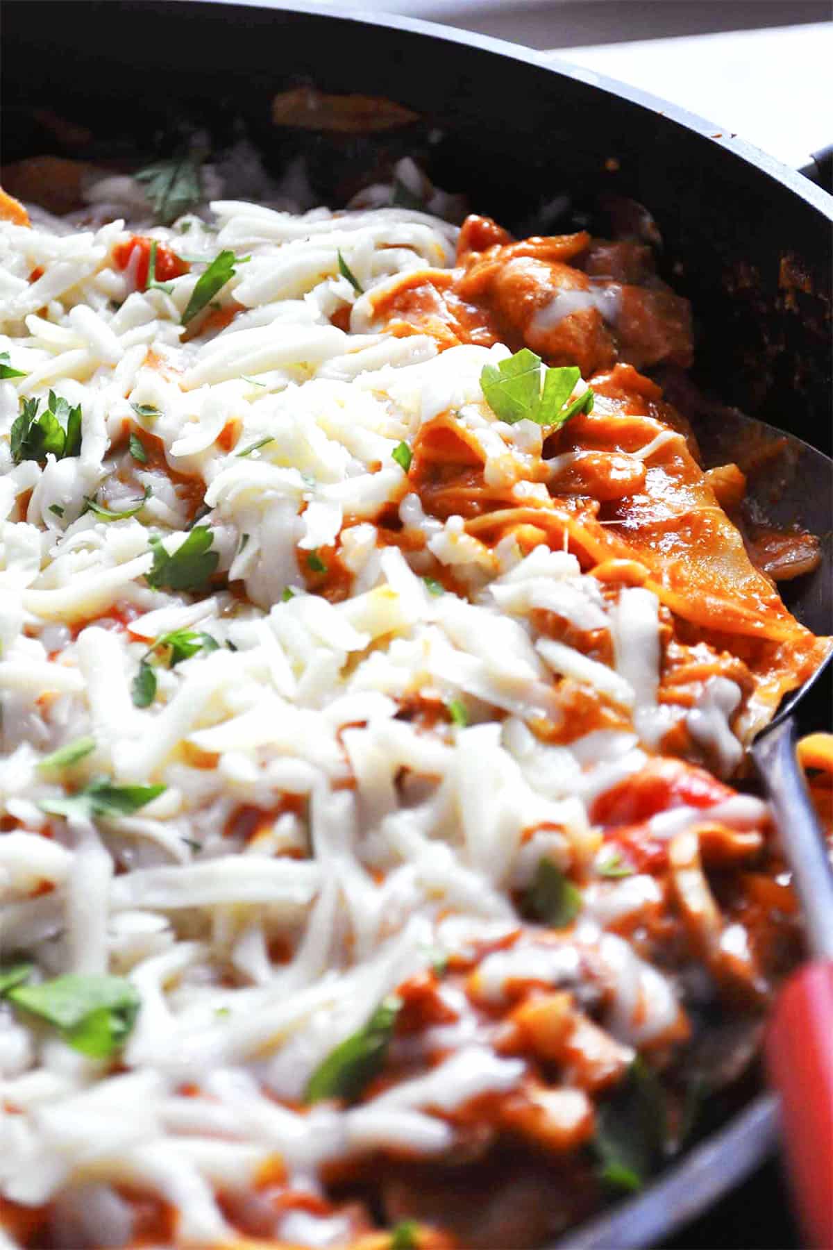 Close-up of skillet lasagna in a pan, topped with melted mozzarella and fresh parsley, featuring visible layers of pasta and rich tomato sauce.