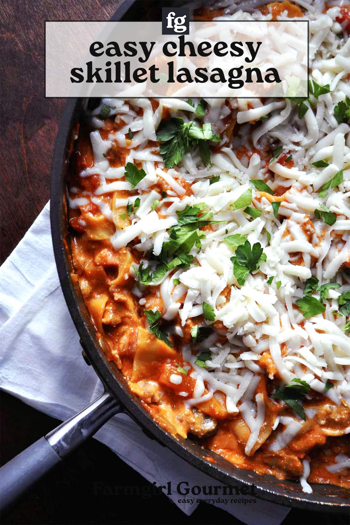 A skillet filled with cheesy skillet lasagna, topped with melted mozzarella and fresh parsley, placed on a dark surface with a white napkin underneath the pan.