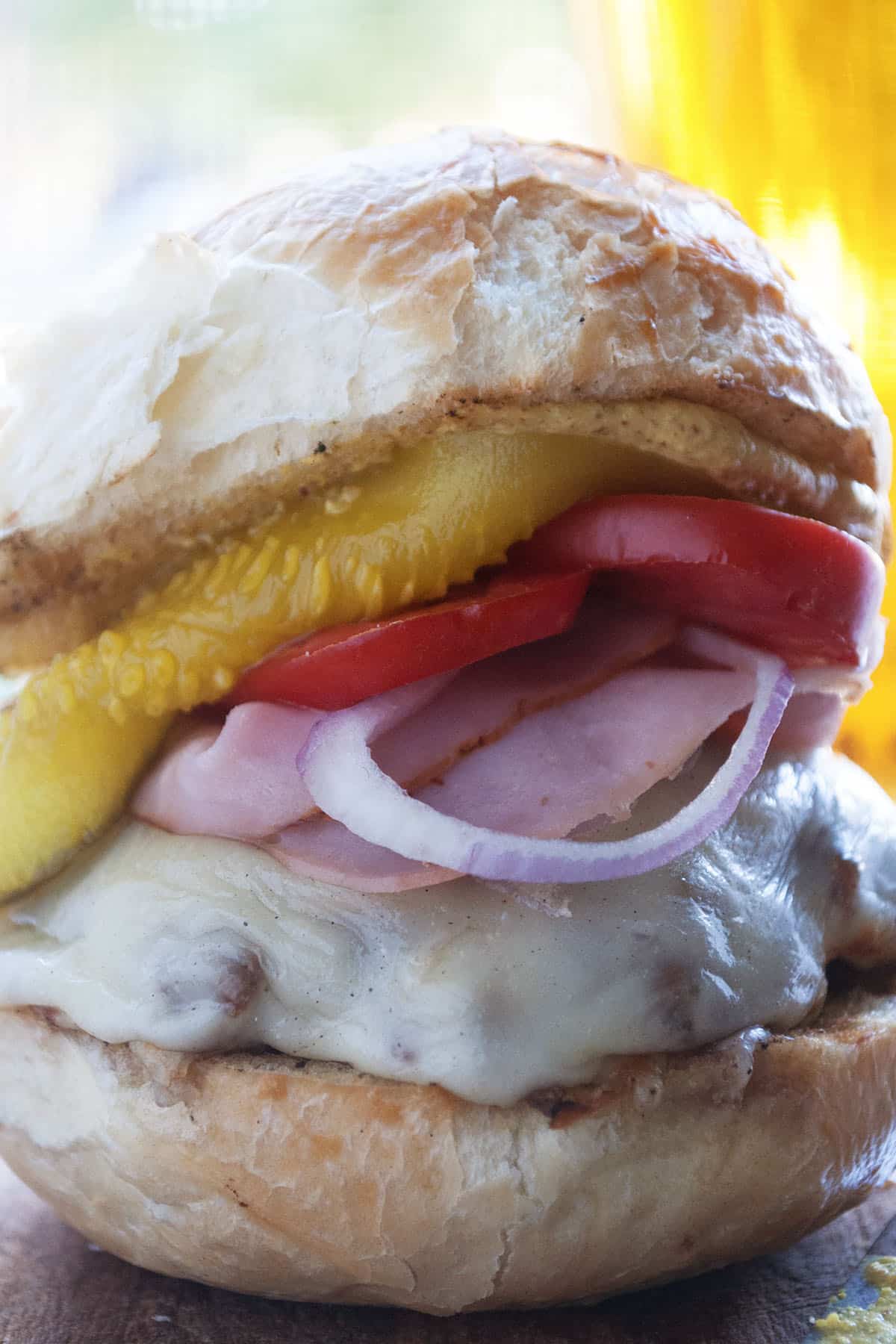 closeup of a cuban burger with ham, tomato, and a pickle