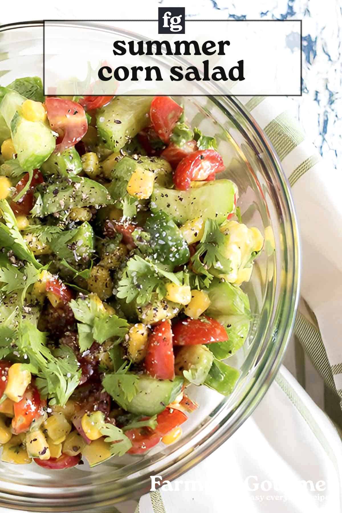 A glass bowl filled with corn avocado cucumber salad featuring sweet corn, creamy avocado, crisp cucumber, cherry tomatoes, cilantro, and black pepper. The image has the text “summer corn salad” at the top.