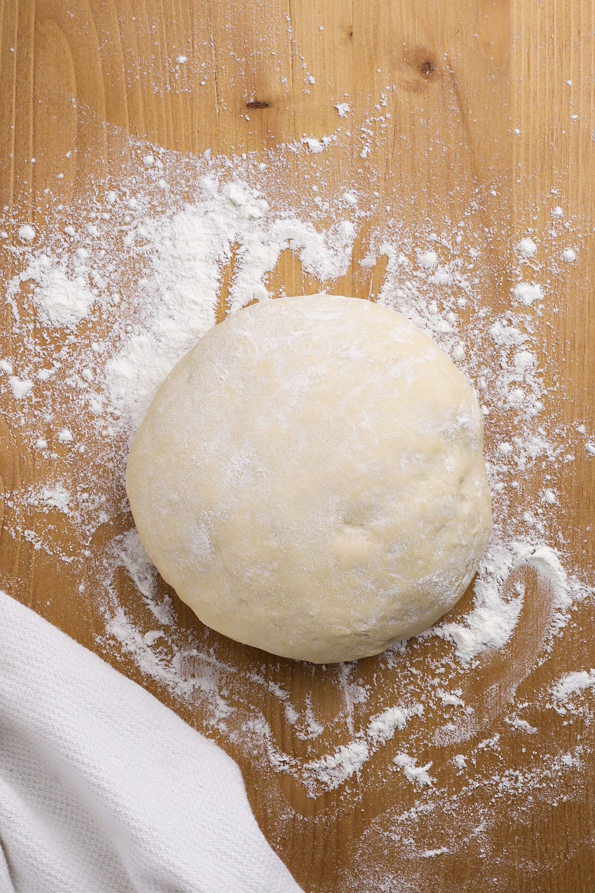 a ball of quick pizza dough on a wood cutting board with flour and a towel.
