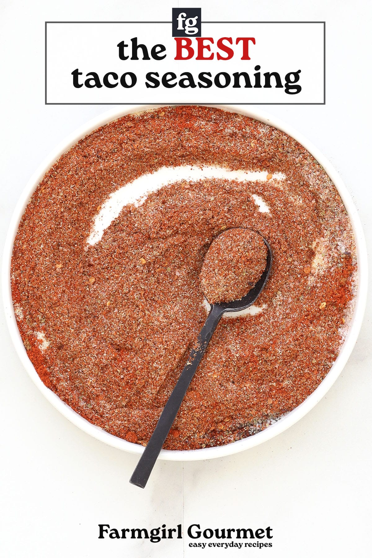 A white bowl filled with homemade taco seasoning and a black spoon, seen from above. Text above reads “the BEST taco seasoning,” and below, “Farmgirl Gourmet easy everyday recipes.”.