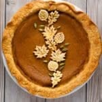 top down view of cardamom pumpkin pie with crust leaves and cardamom pods