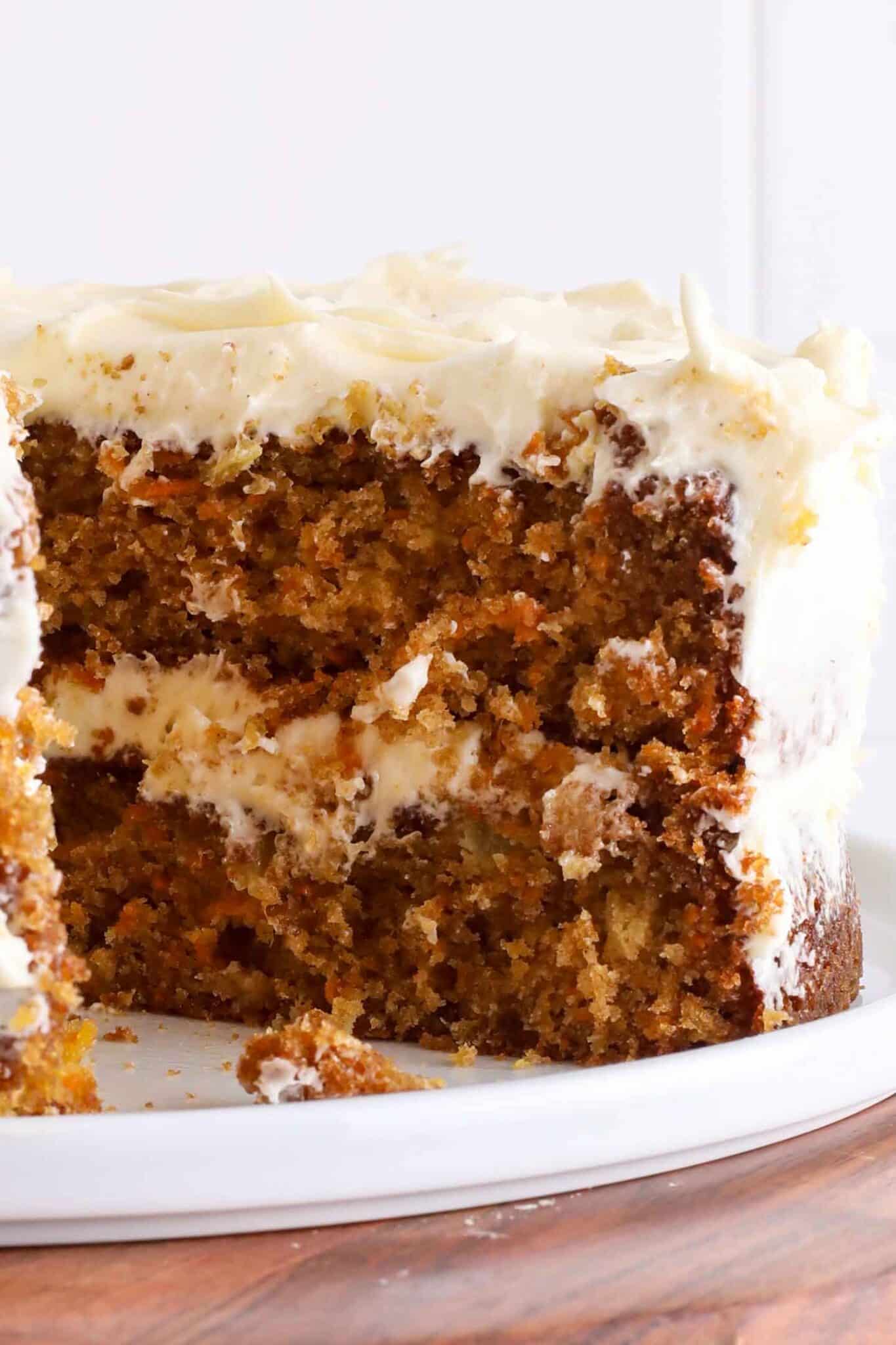 A close-up of a sliced carrot cake with cream cheese frosting, showing its moist, textured interior and layers of frosting on a white plate—truly the best carrot cake recipe brought to life.