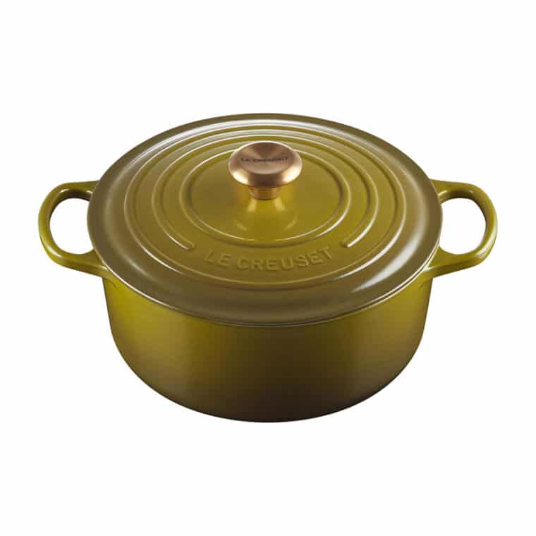 A round, green enameled cast iron Dutch oven with two handles and a gold knob on the lid. The brand name Le Creuset is embossed on the lid.