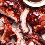 Barbecued ribs with a glossy, caramelized sauce—truly the best BBQ'd ribs—are arranged on a tray. A basting brush and a small bowl of barbecue sauce sit in the corner. The ribs look juicy and tender.