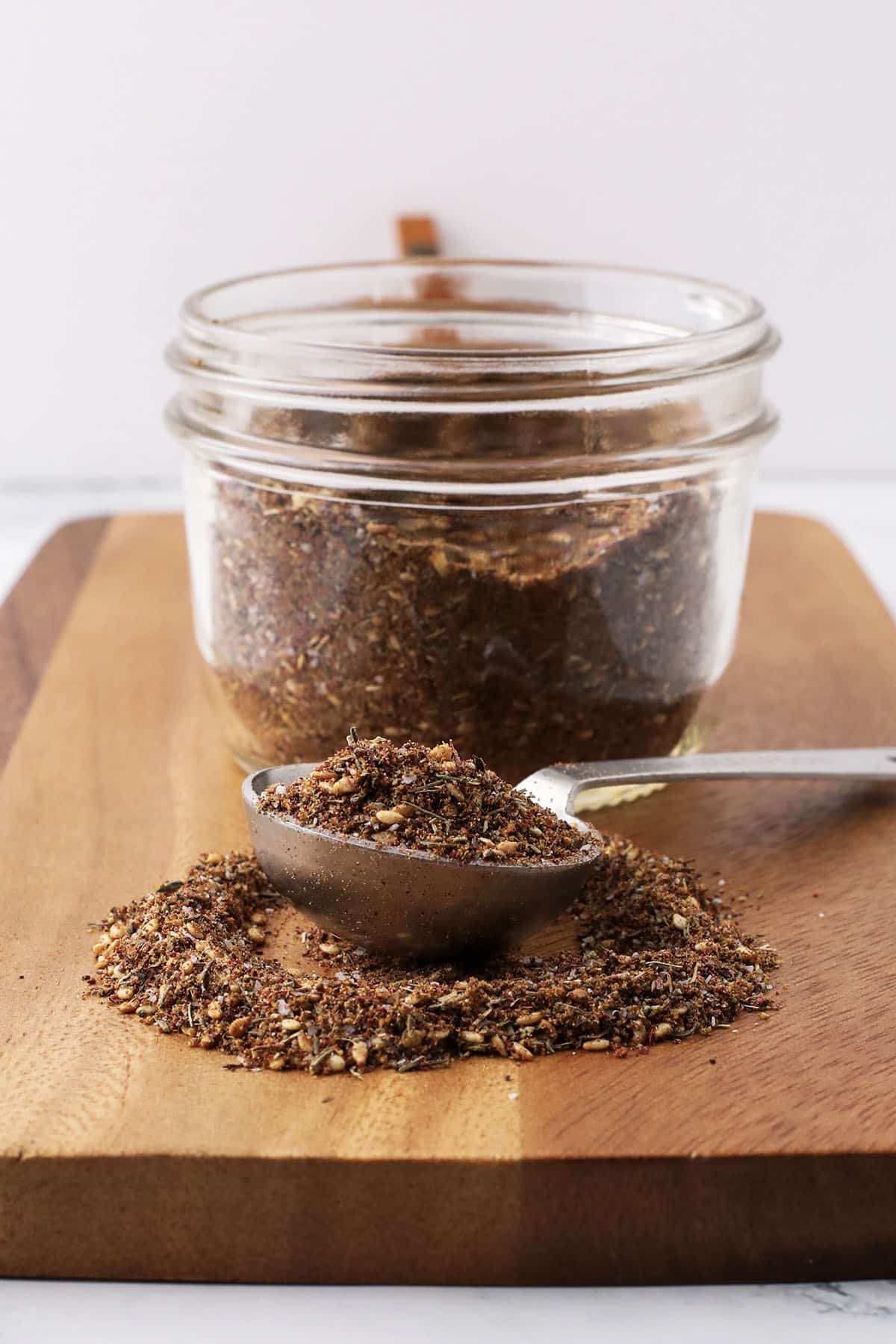 Small glass jar filled with Za’atar blend on a wood surface