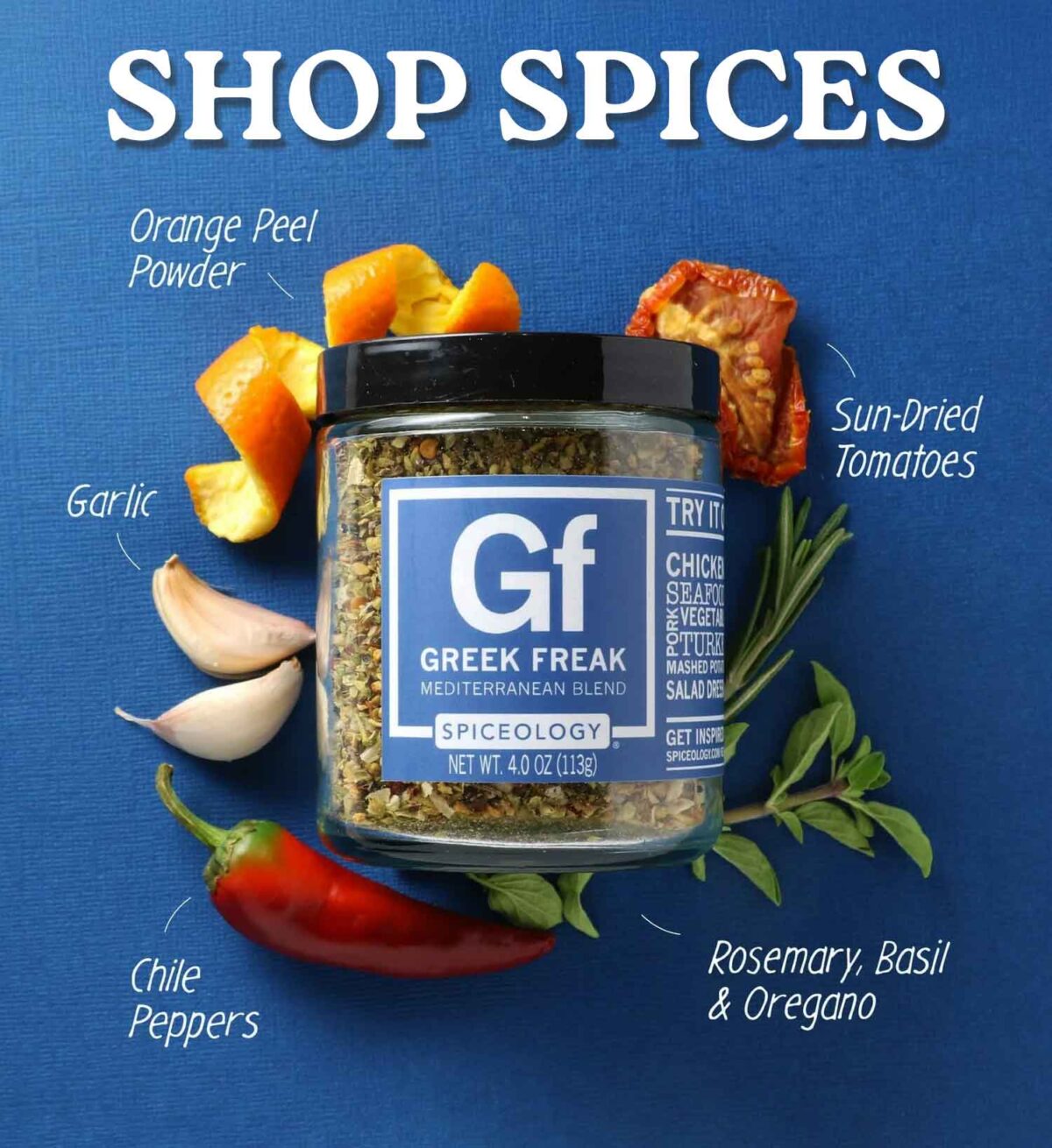 A jar of Greek Freak Mediterranean Blend spice sits on a blue background, surrounded by labeled ingredients: orange peel powder, sun-dried tomatoes, garlic, chile peppers, and rosemary, basil & oregano.