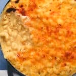 A close-up of a baked macaroni and cheese dish in a round pan, with a golden-brown cheesy crust on top and a creamy macaroni filling visible where a portion has been scooped out.