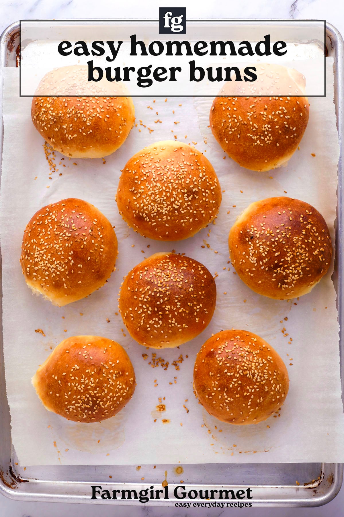 A baking tray lined with parchment paper holds eight golden brown, sesame-topped fluffy hamburger buns. Text above reads, easy homemade burger buns, with Farmgirl Gourmet at the bottom.
