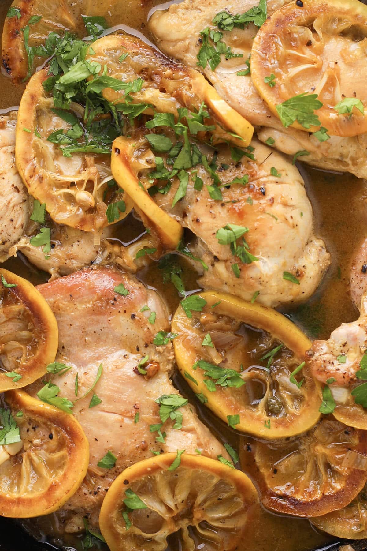 Chicken breasts cooked in a golden lemon chicken piccata sauce, garnished with chopped parsley and topped with slices of lemon. The dish appears juicy and flavorful, with vibrant yellow and green colors.
