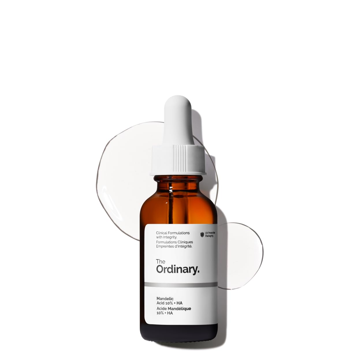 A brown glass dropper bottle of The Ordinary Mandelic Acid 10% + HA serum, shown with the white label facing forward and some serum drops around the bottle on a white background.