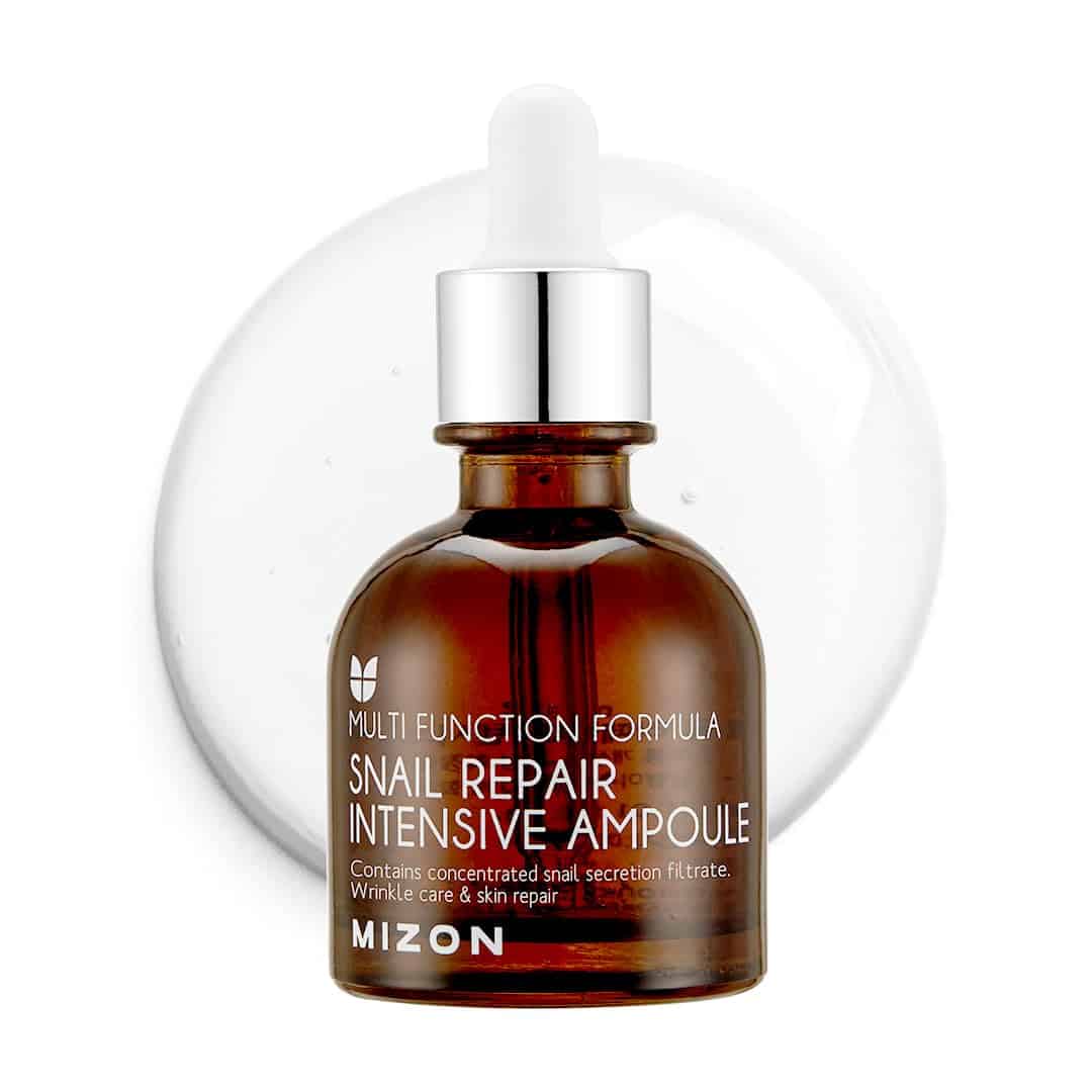 A brown glass dropper bottle labeled Mizon Snail Repair Intensive Ampoule sits in front of a clear liquid drop. The label highlights wrinkle care and skin repair benefits.