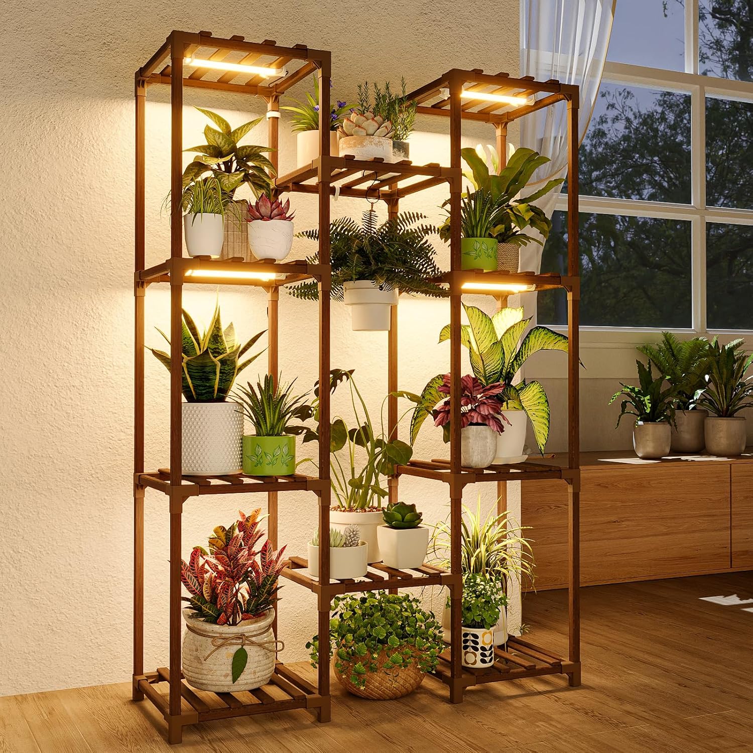 Tall wooden plant stands with multiple shelves hold various potted plants. Warm lights illuminate the plants. The stands are near a large window with curtains, and a wooden cabinet is in the background.
