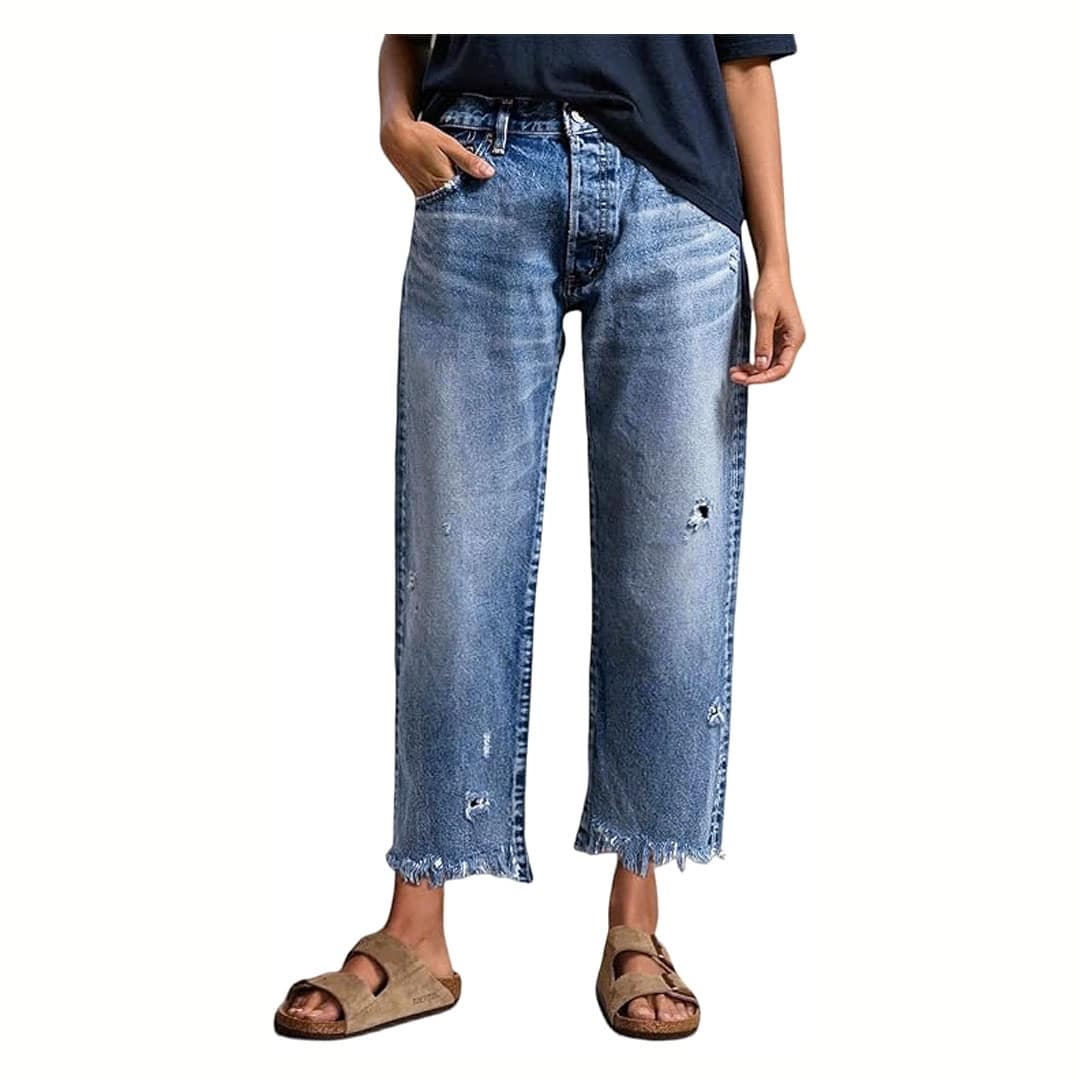 Person wearing a dark t-shirt, loose-fitting blue distressed jeans with frayed hems, and brown sandals. The image is cropped from the shoulders down, and the person has one hand in their pocket.