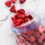 Sliced strawberries in a resealable plastic bag on a marble surface, with a few pieces scattered outside the bag.