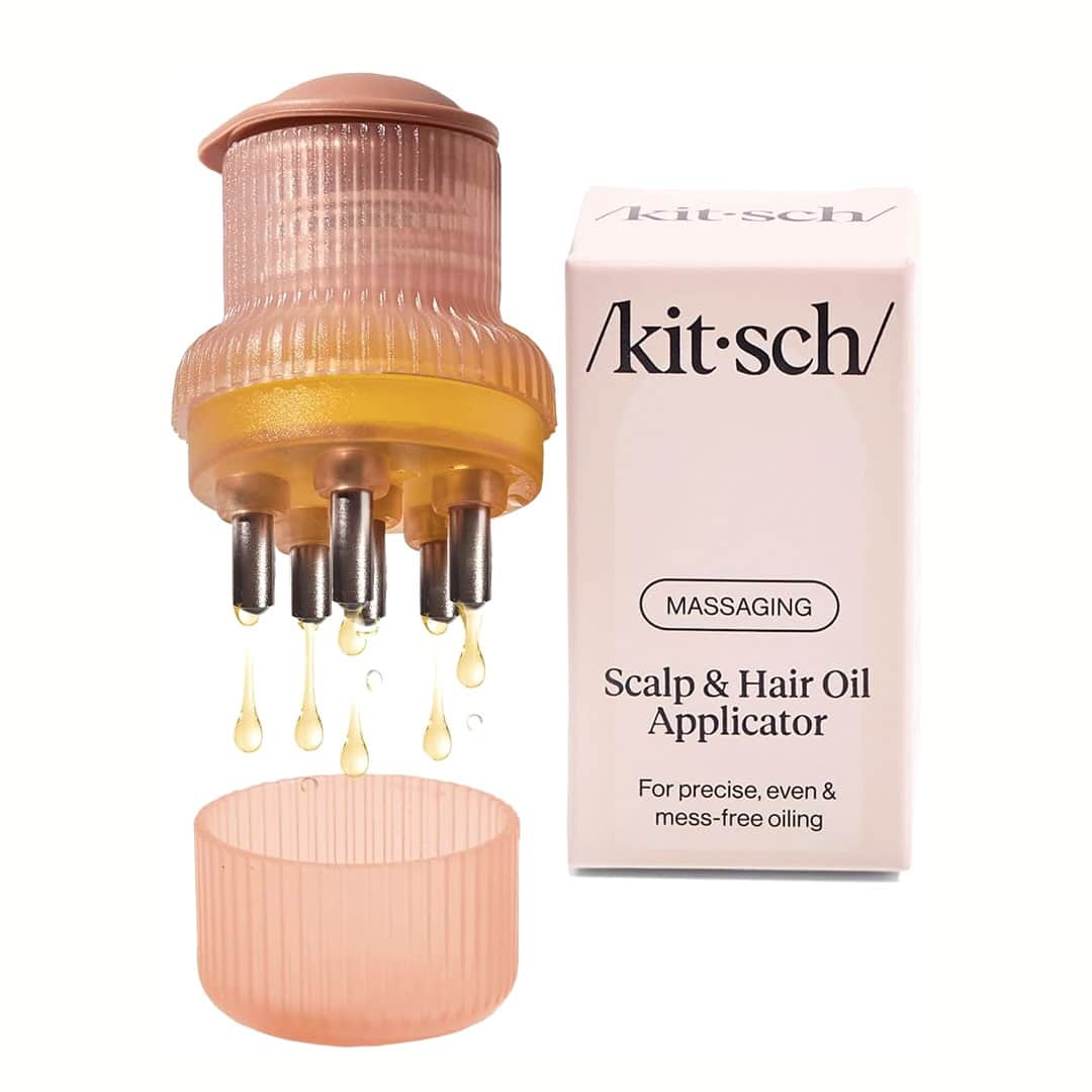 A pink scalp and hair oil applicator with metal tips dispenses oil drops. Next to it is a matching cap and a box labeled “/kit·sch/ Massaging Scalp & Hair Oil Applicator.”.