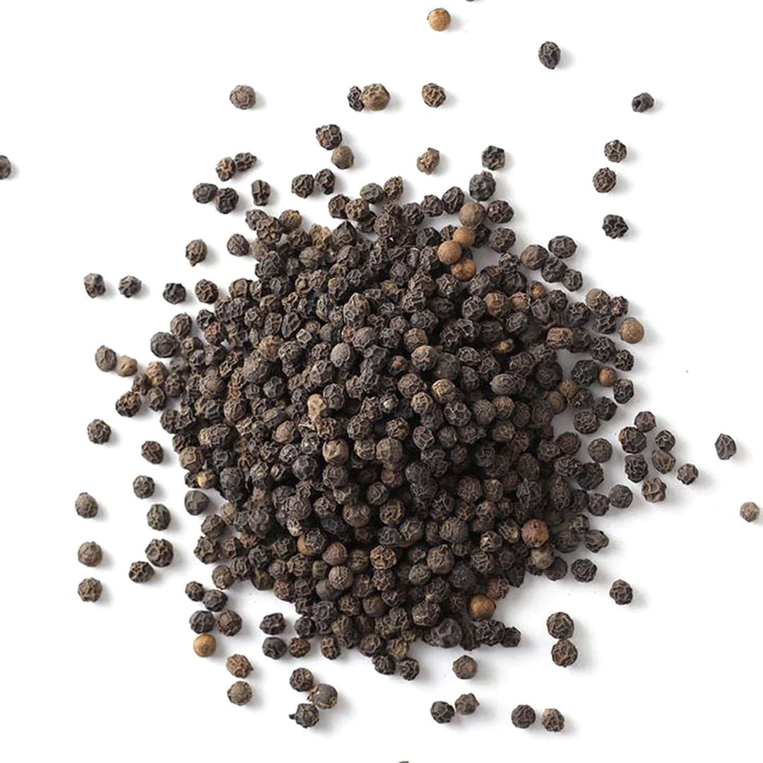 A pile of whole black peppercorns is scattered on a white background, with some peppercorns spread out around the main cluster.