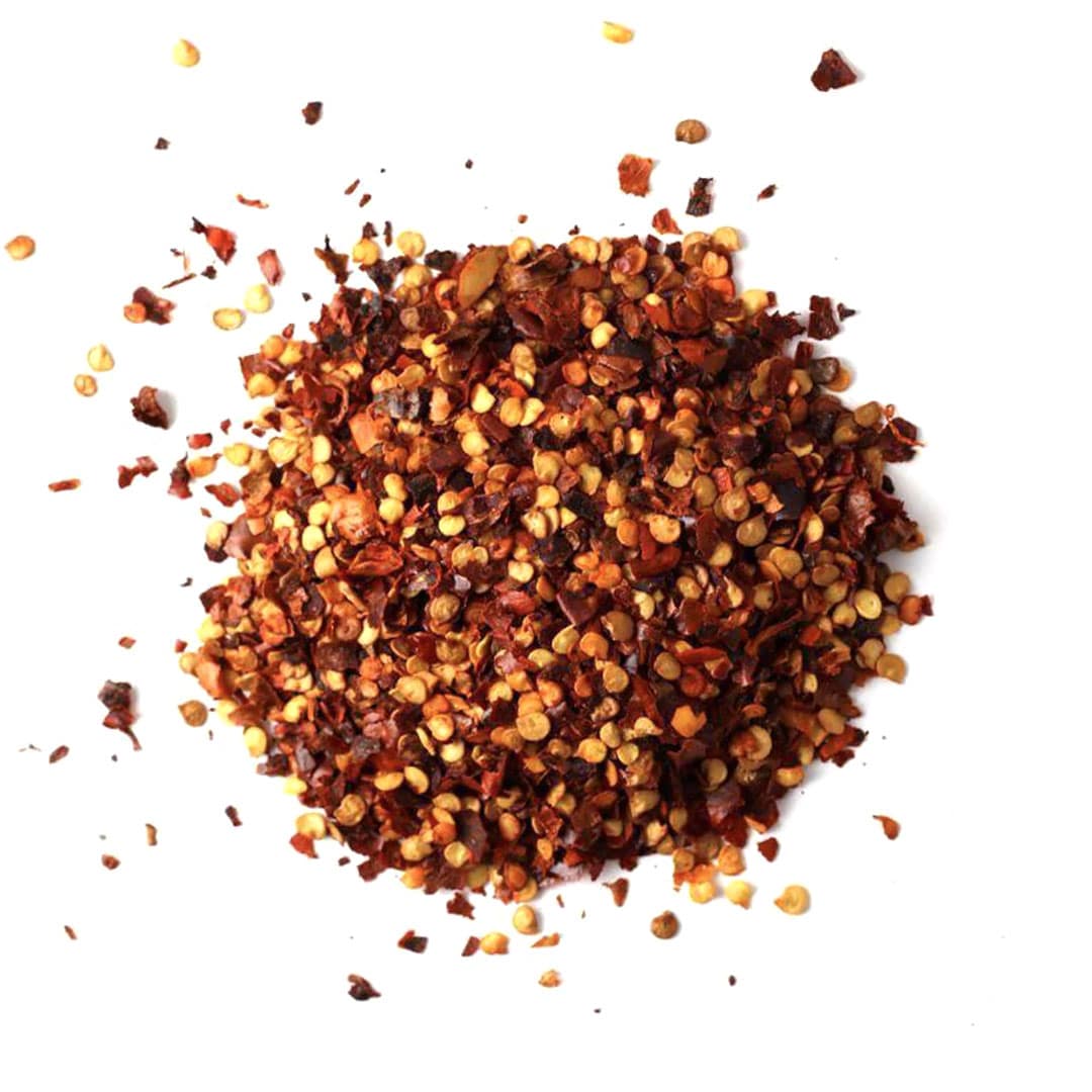 A pile of crushed red pepper flakes scattered on a white background.