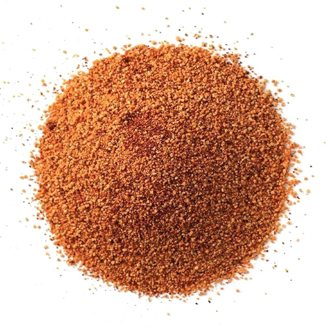 A mound of finely ground, reddish-brown seasoning or spice blend scattered on a white background.