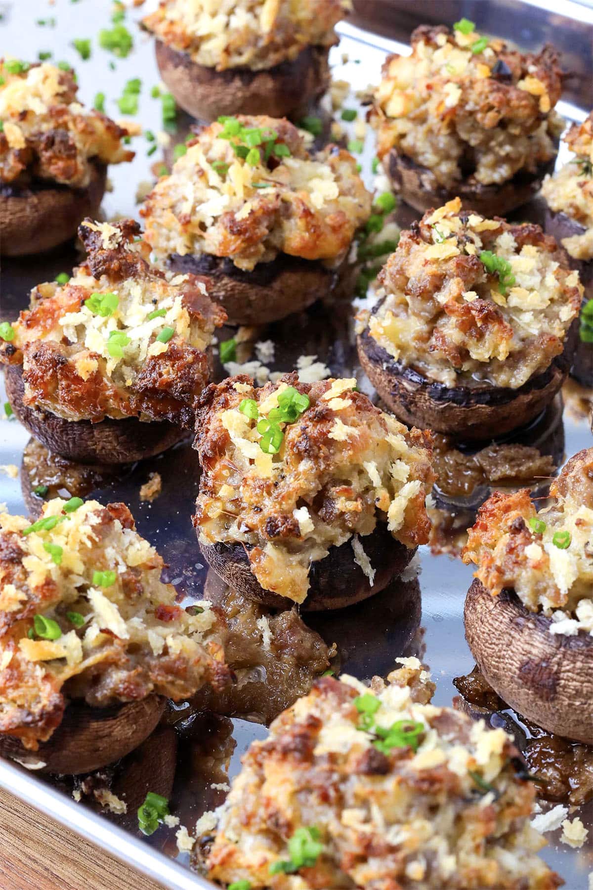 Stuffed mushrooms topped with a golden, crispy breadcrumb mixture, garnished with chopped green herbs, are arranged on a metal baking tray. The filling appears savory and slightly browned from baking.